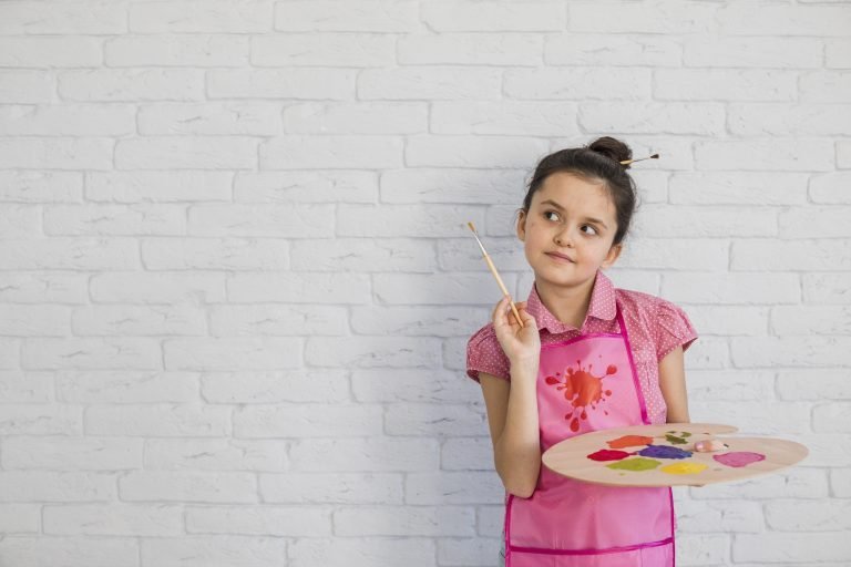 portrait-girl-with-paintbrush-palette-standing-against-white-wall