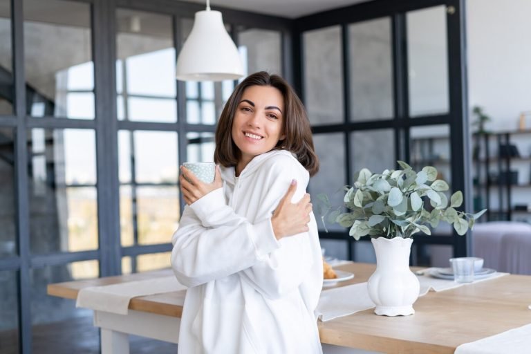 young-woman-warm-white-hoodie-home-kitchen-starts-her-day-with-cup-coffee_343596-7222
