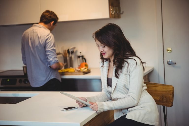 Woman using digital tablet while man working in background at kitchen
