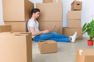 Man using a laptop surrounded by a pile of boxes.