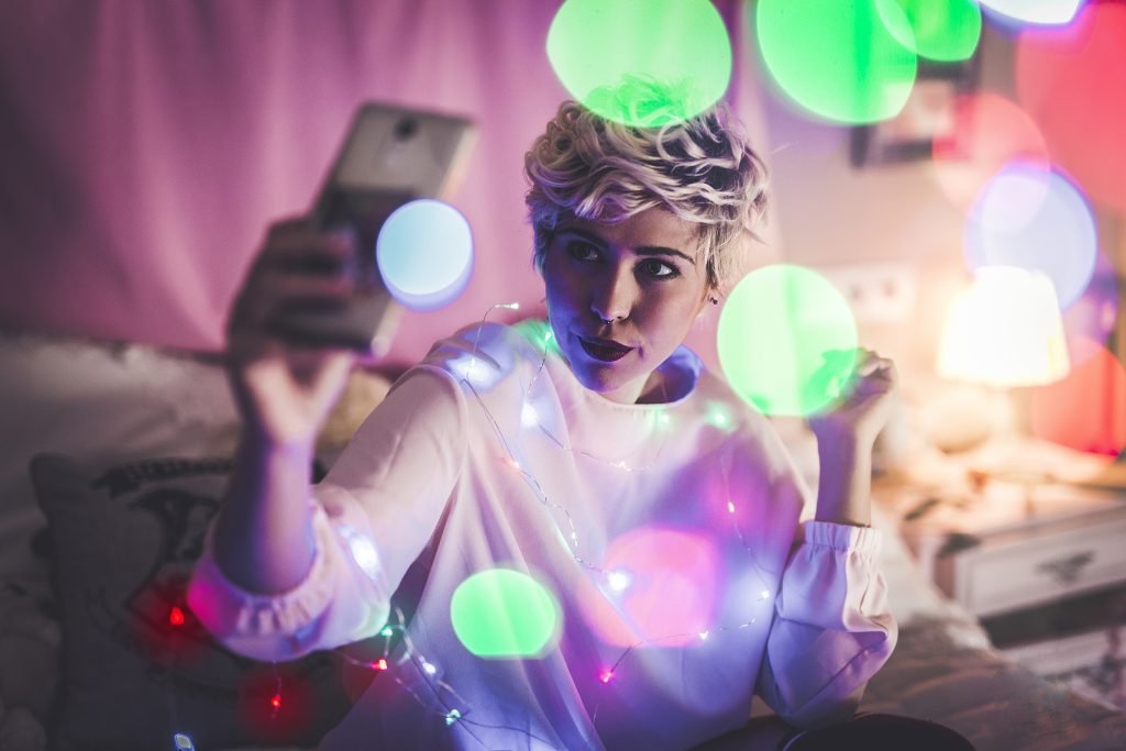 Young female taking a selfie in her room with Christmas lights