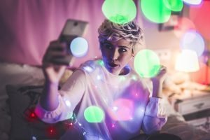 Young female taking a selfie in her room with Christmas lights