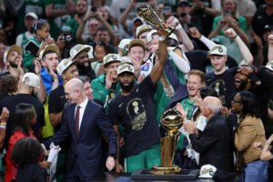 Jaylen Brown holds up the NBA Finals MVP trophy while surrounded by teammates, coaches, and fans celebrating the Boston Celtics' championship victory. LandonBuford