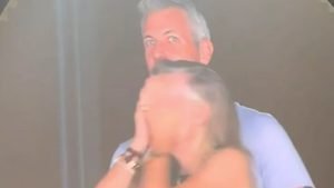 Astronomer CEO Andy Byron with gray hair looking directly into the camera while standing behind Kristin Cabot who is covering her face with her hands, both caught under bright stadium lighting.