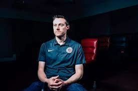 Trent Redden, General Manager of the Los Angeles Clippers, sits in a dimly lit room wearing team-branded apparel, focused and composed, symbolizing his strategic leadership behind the team’s rise. LandonBuford.com