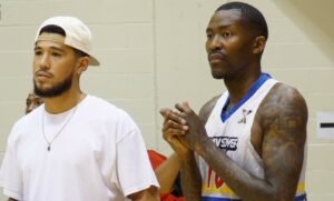 Devin Booker smiles courtside while watching a game at The CrawsOver Pro-Am in Seattle, showcasing his support for Jamal Crawford’s community basketball event.